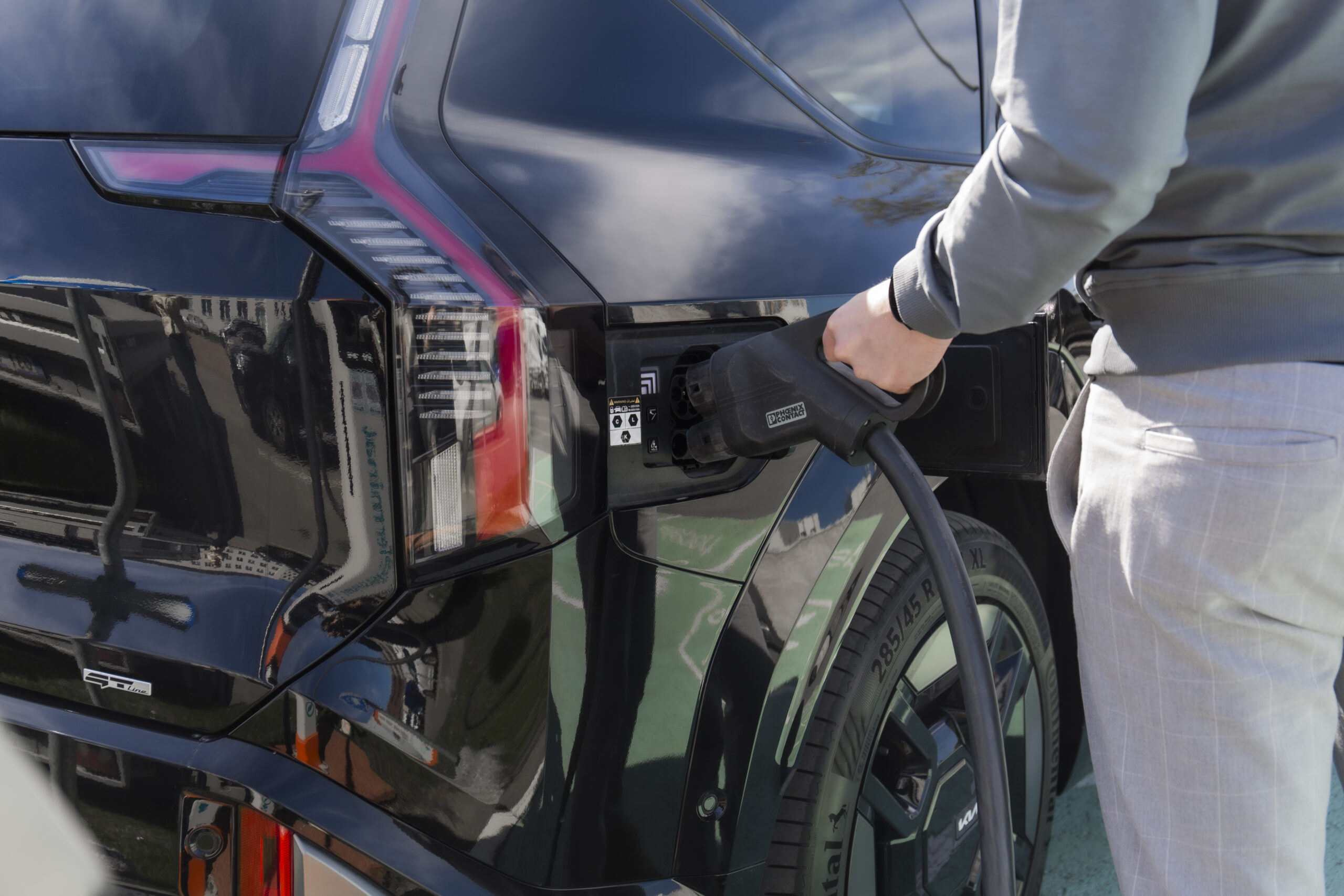 cilvēks liek elektroauto lādēties