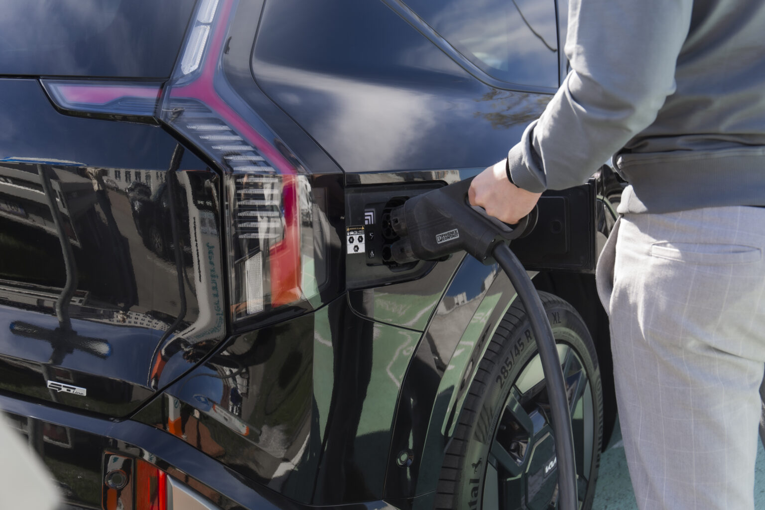 cilvēks liek elektroauto lādēties